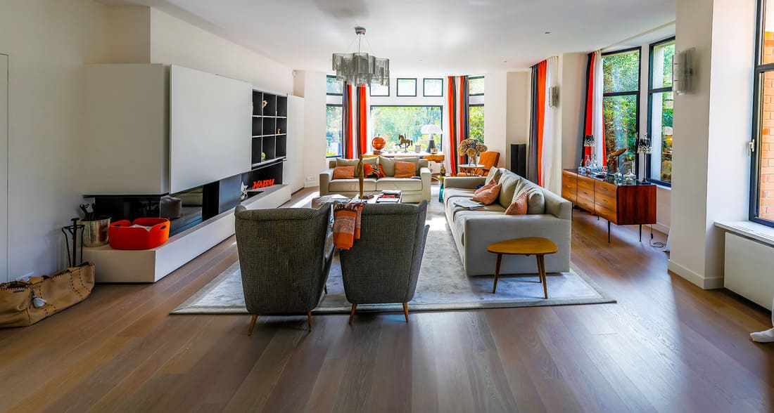 Grand salon avec plusieurs canapés blanc, et fauteuils gris foncés, grand tapis au sol, rideaux gris orange et blanc